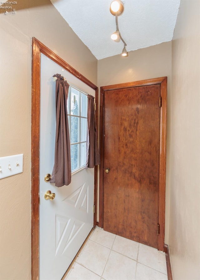 doorway to outside with a textured ceiling, rail lighting, and light tile patterned floors