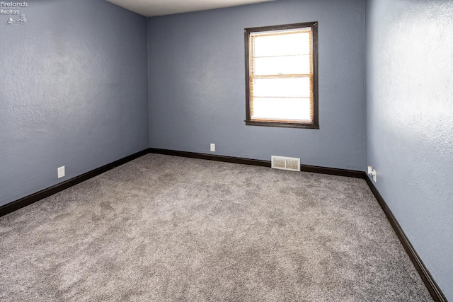 carpeted spare room with baseboards, visible vents, and a textured wall