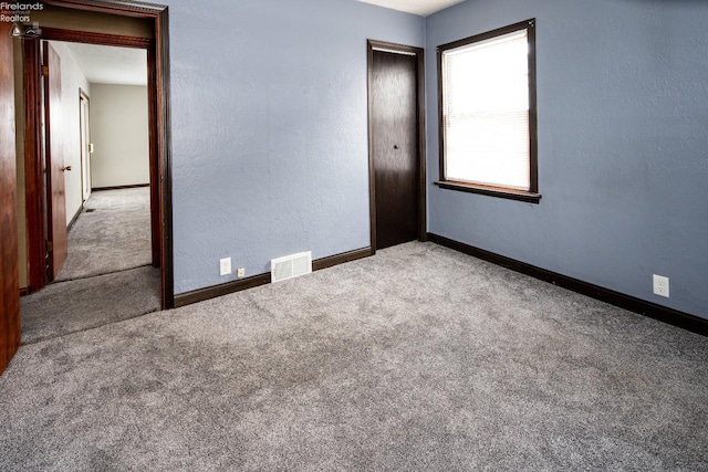 spare room featuring a textured wall, carpet floors, visible vents, and baseboards