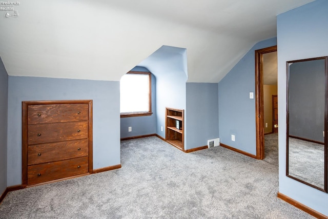 additional living space featuring lofted ceiling, light colored carpet, visible vents, and baseboards