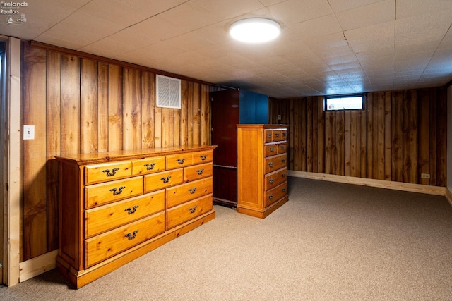 basement featuring light carpet, visible vents, and wooden walls