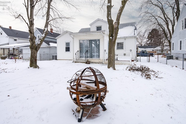 snow covered back of property featuring entry steps, central AC unit, and fence