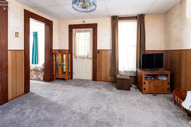 living room with a paneled ceiling, light carpet, and wood walls