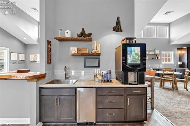 kitchen with high vaulted ceiling, sink, stainless steel fridge, dark brown cabinets, and light hardwood / wood-style flooring