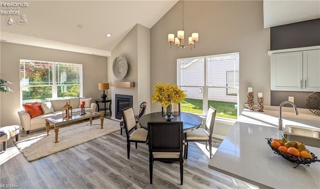 dining space with high vaulted ceiling, light wood-type flooring, sink, and a fireplace