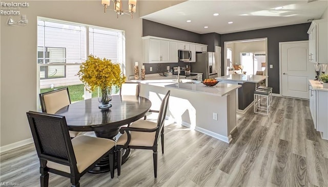 kitchen with an inviting chandelier, light hardwood / wood-style flooring, stainless steel appliances, a kitchen island with sink, and white cabinets