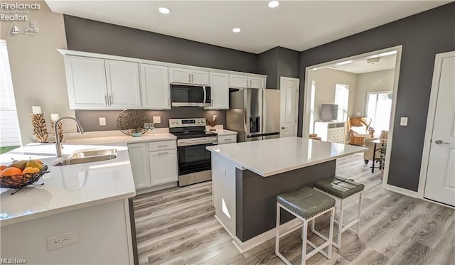 kitchen with stainless steel appliances, sink, white cabinets, and light hardwood / wood-style floors