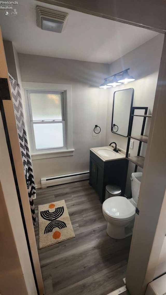 bathroom featuring wood-type flooring, toilet, vanity, and a baseboard heating unit