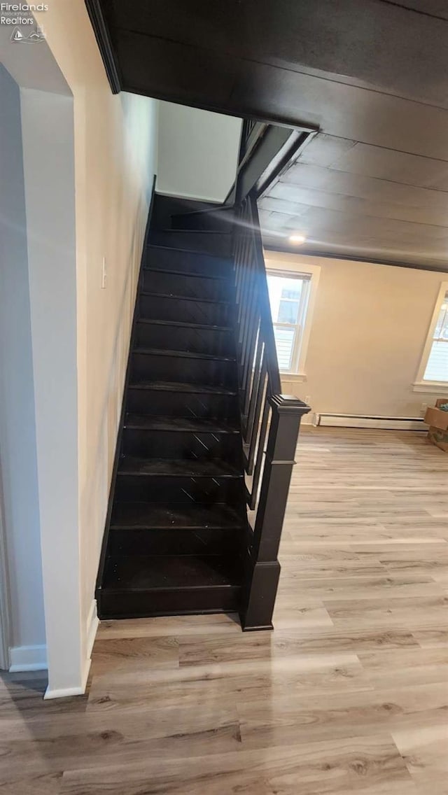 stairs featuring wood-type flooring and a baseboard heating unit