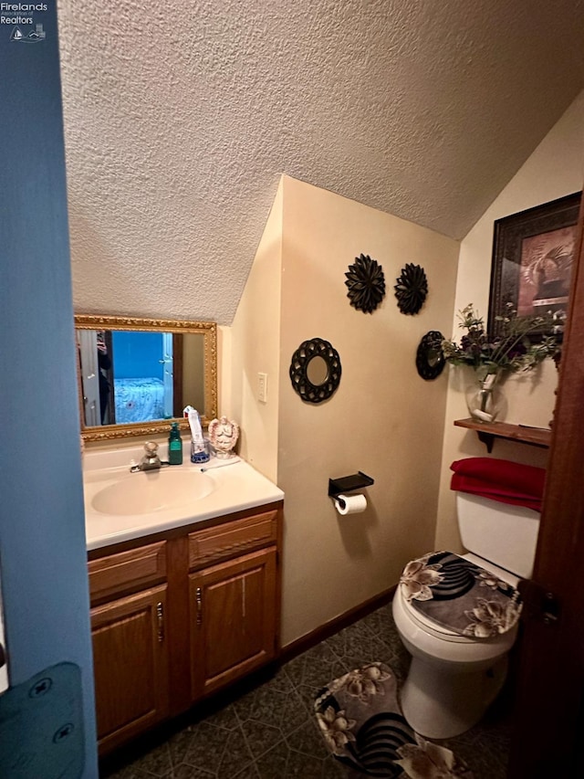 bathroom with toilet, vaulted ceiling, a textured ceiling, vanity, and tile patterned flooring