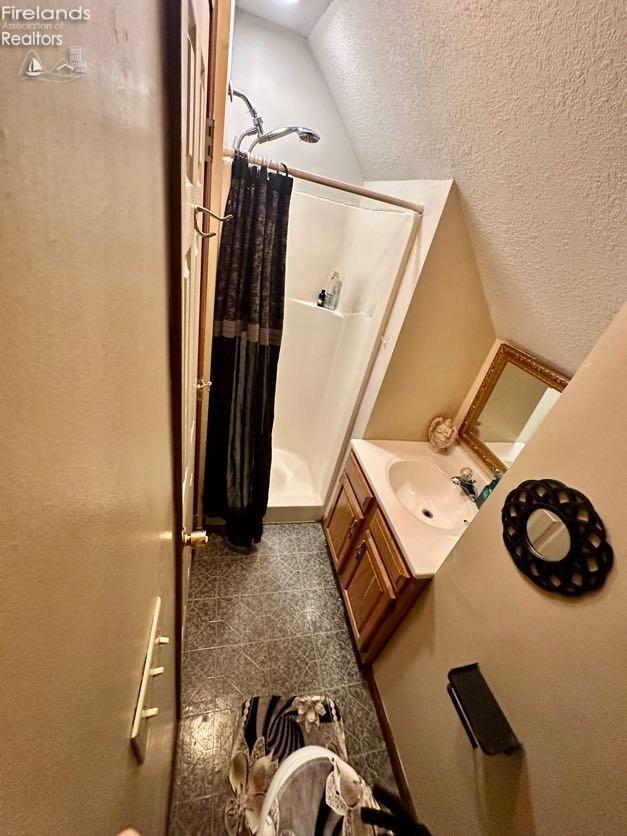 bathroom featuring walk in shower, vanity, vaulted ceiling, and a textured ceiling