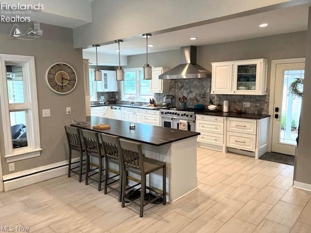 kitchen with white cabinets, a kitchen bar, range with two ovens, kitchen peninsula, and wall chimney range hood