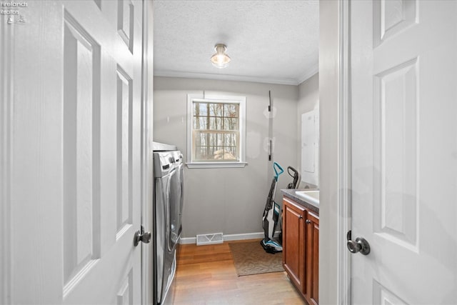 laundry room with independent washer and dryer, ornamental molding, light hardwood / wood-style flooring, and a textured ceiling