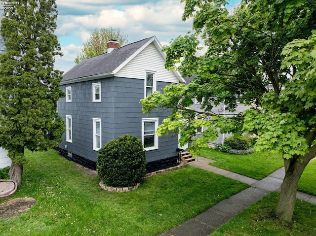 view of side of home featuring entry steps, a chimney, a lawn, and roof with shingles