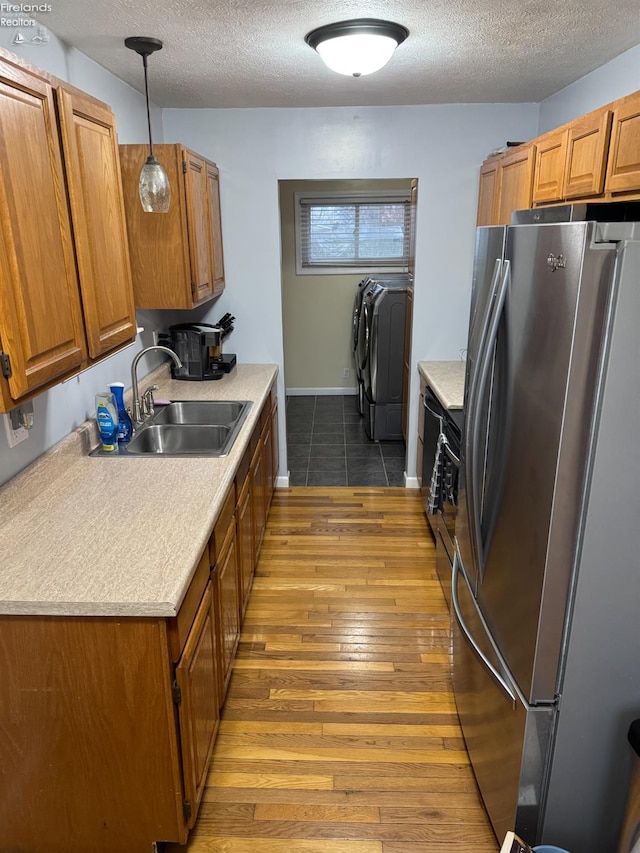 kitchen with sink, stainless steel refrigerator, pendant lighting, independent washer and dryer, and hardwood / wood-style floors