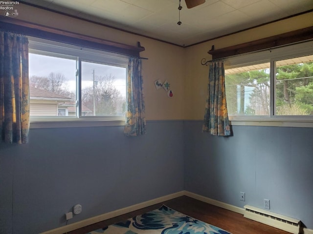 spare room with baseboards, baseboard heating, and dark wood-type flooring
