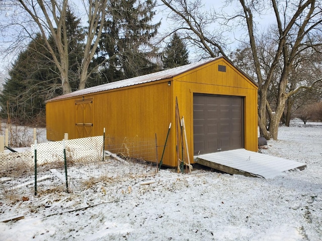 snow covered garage with a detached garage and fence