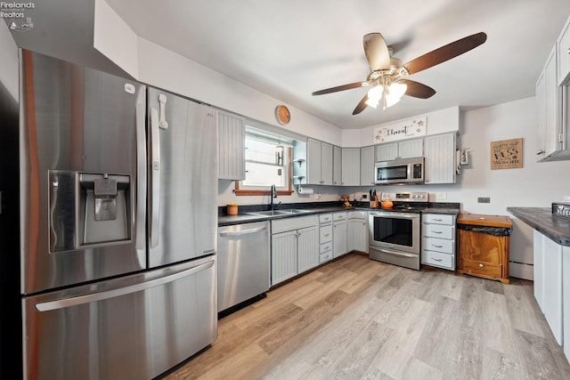 kitchen with gray cabinets, appliances with stainless steel finishes, sink, ceiling fan, and light hardwood / wood-style flooring