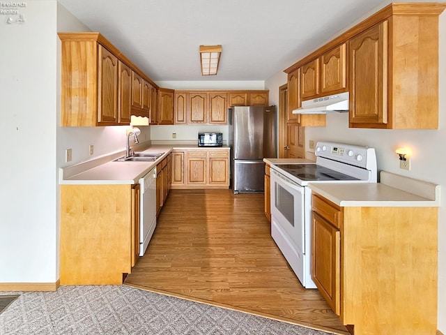 kitchen with under cabinet range hood, white appliances, a sink, light countertops, and light wood-type flooring