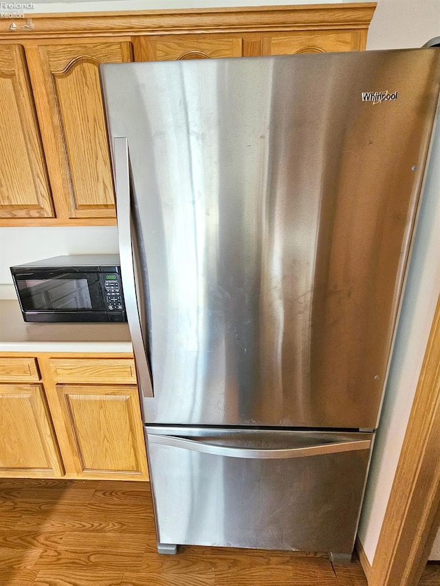 kitchen featuring freestanding refrigerator, black microwave, light countertops, and wood finished floors