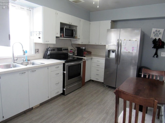 kitchen featuring appliances with stainless steel finishes, sink, white cabinetry, and light wood-type flooring