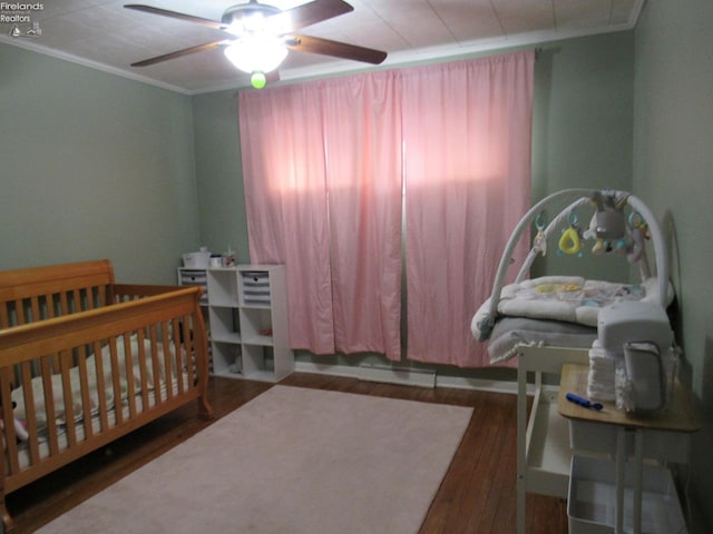 bedroom with ceiling fan, crown molding, dark hardwood / wood-style flooring, and a nursery area