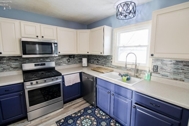 kitchen featuring blue cabinets, stainless steel appliances, a sink, light wood-style floors, and light countertops