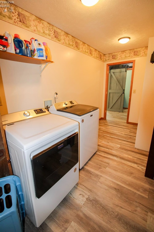 clothes washing area with washing machine and dryer, light wood-style flooring, a textured ceiling, and a barn door