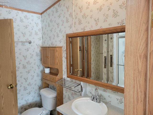 half bathroom featuring a textured ceiling, toilet, vanity, ornamental molding, and wallpapered walls