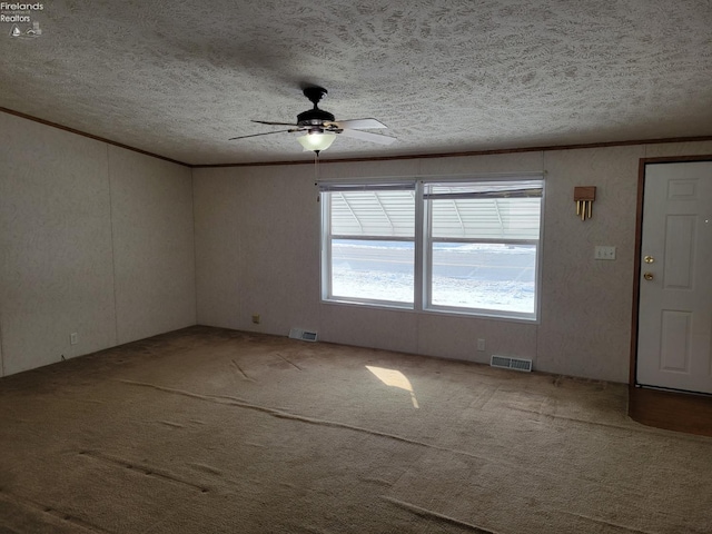 spare room with a textured ceiling, carpet floors, visible vents, and crown molding