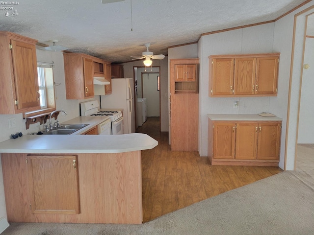 kitchen with a textured ceiling, a peninsula, white appliances, a sink, and light countertops