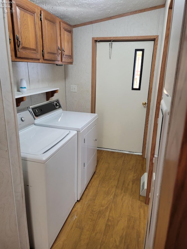 laundry area with light wood finished floors, cabinet space, ornamental molding, washing machine and dryer, and a textured ceiling