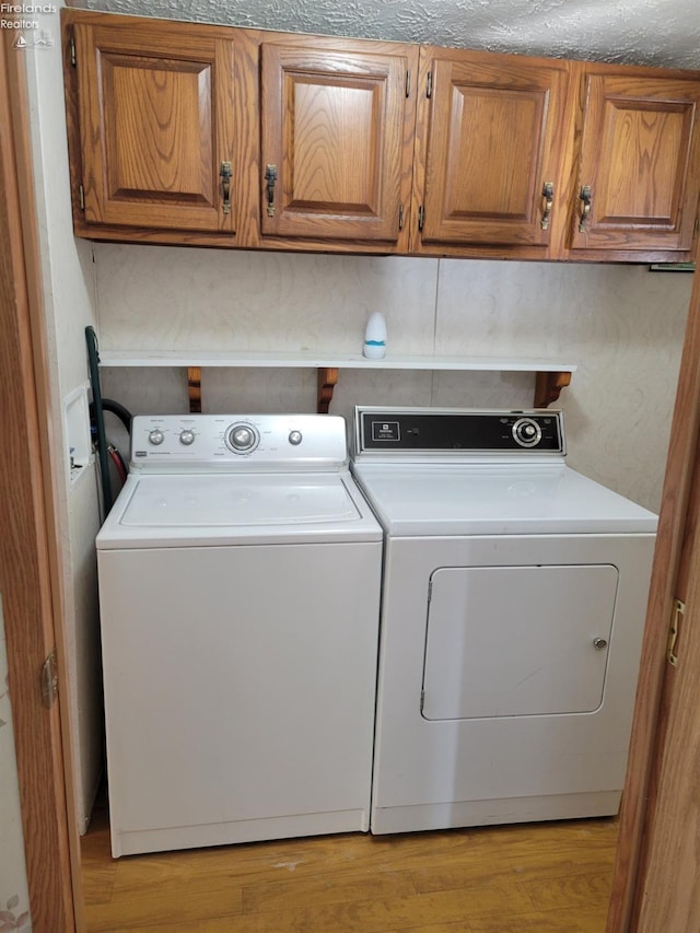 washroom featuring light wood-style flooring, cabinet space, and washer and clothes dryer