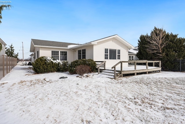 snow covered back of property with fence and a deck