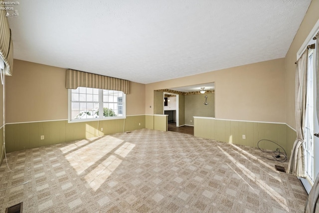 empty room with wainscoting, visible vents, carpet flooring, and a textured ceiling