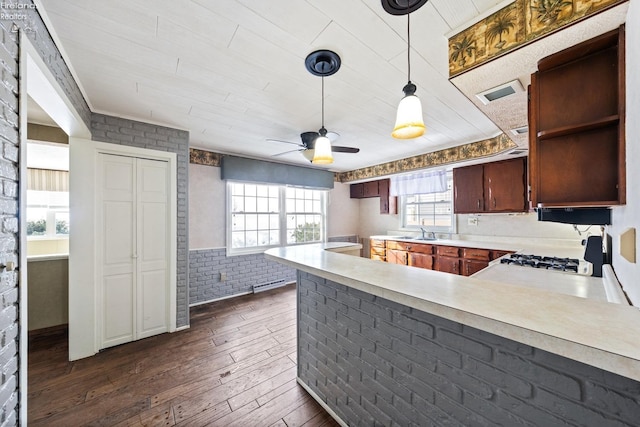 kitchen with brick wall, stove, dark wood-style flooring, light countertops, and a sink