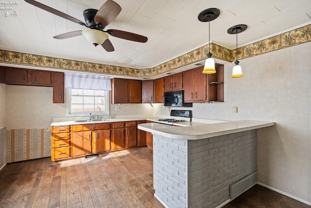 kitchen with range, a peninsula, light countertops, black microwave, and a sink