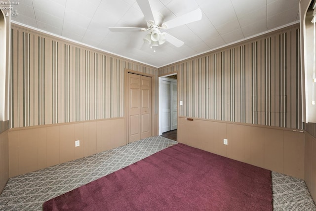 empty room featuring a wainscoted wall, carpet flooring, ceiling fan, and wallpapered walls