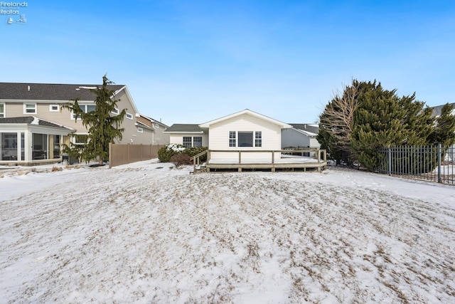 snow covered back of property featuring a deck, a sunroom, fence, and a residential view