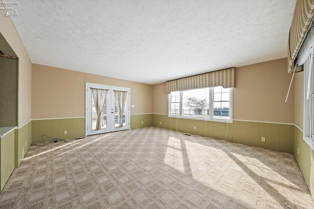 empty room with light colored carpet, a textured ceiling, and wainscoting