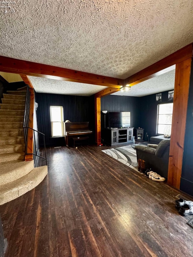 unfurnished living room with a textured ceiling, dark wood-style flooring, stairway, beamed ceiling, and plenty of natural light