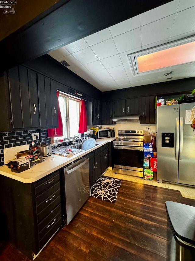 kitchen featuring tasteful backsplash, dark wood-style floors, stainless steel appliances, light countertops, and under cabinet range hood