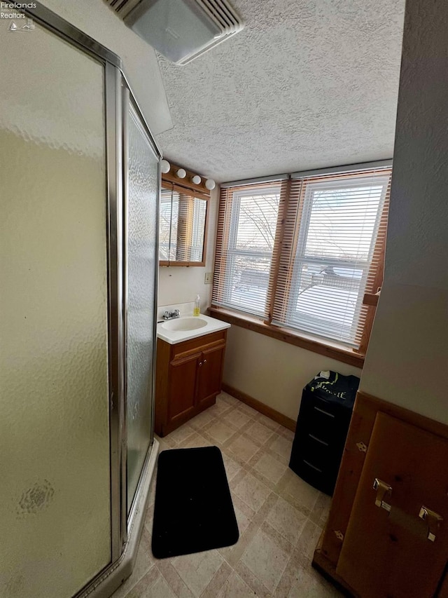 full bathroom with a stall shower, vanity, a textured ceiling, baseboards, and tile patterned floors