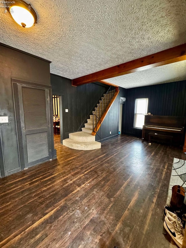 interior space with dark wood-style floors, a textured ceiling, stairway, and beam ceiling