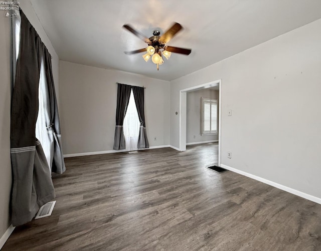 spare room with dark wood-style floors, baseboards, visible vents, and a ceiling fan