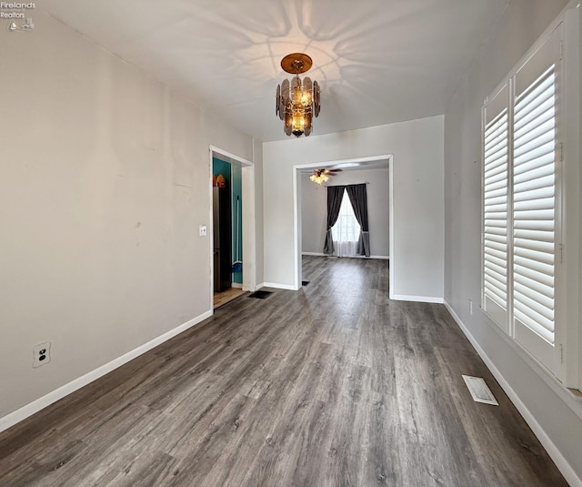 unfurnished dining area with ceiling fan with notable chandelier, dark wood-style flooring, visible vents, and baseboards