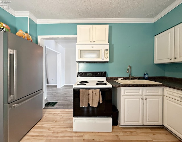 kitchen with electric stove, dark countertops, white microwave, freestanding refrigerator, and a sink