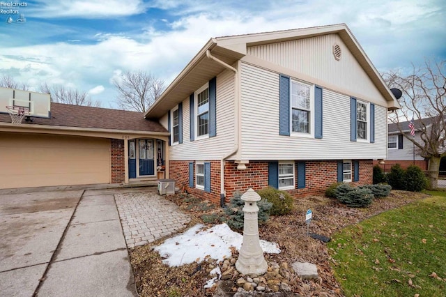 split level home with concrete driveway, brick siding, and an attached garage