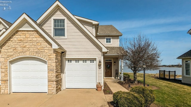 view of front of home featuring a shingled roof, a water view, driveway, stone siding, and a front lawn