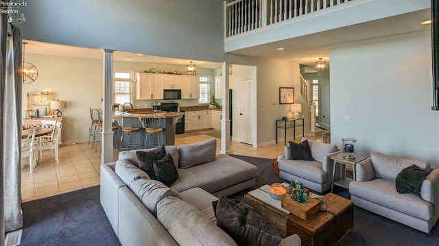 living room with light tile patterned floors, a towering ceiling, decorative columns, and baseboards